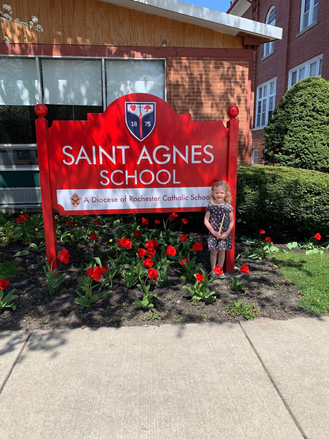 St. Agnes School student, Evie, stands by her school sign.